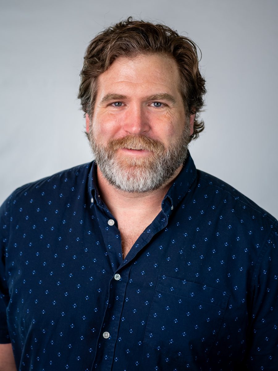Headshot of a bearded man in a navy shirt on a light grey backdrop
