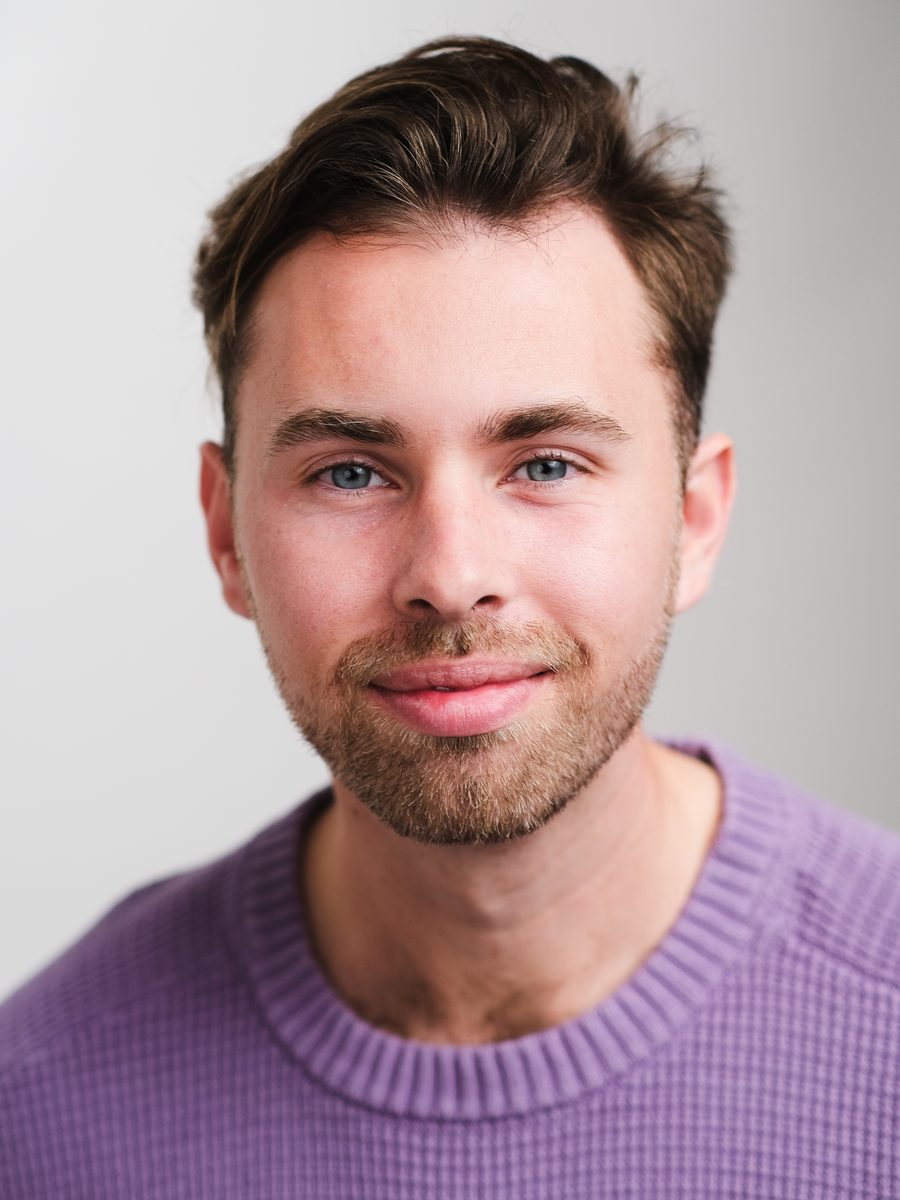 Headshot of a smiling man in a purple sweater