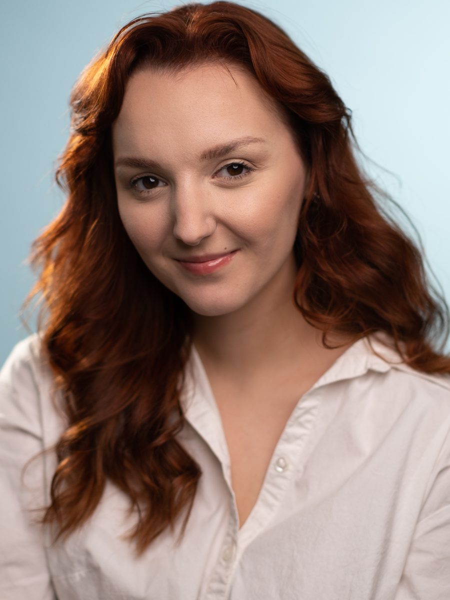 Headshot of a woman with red hair on a light blue backdrop