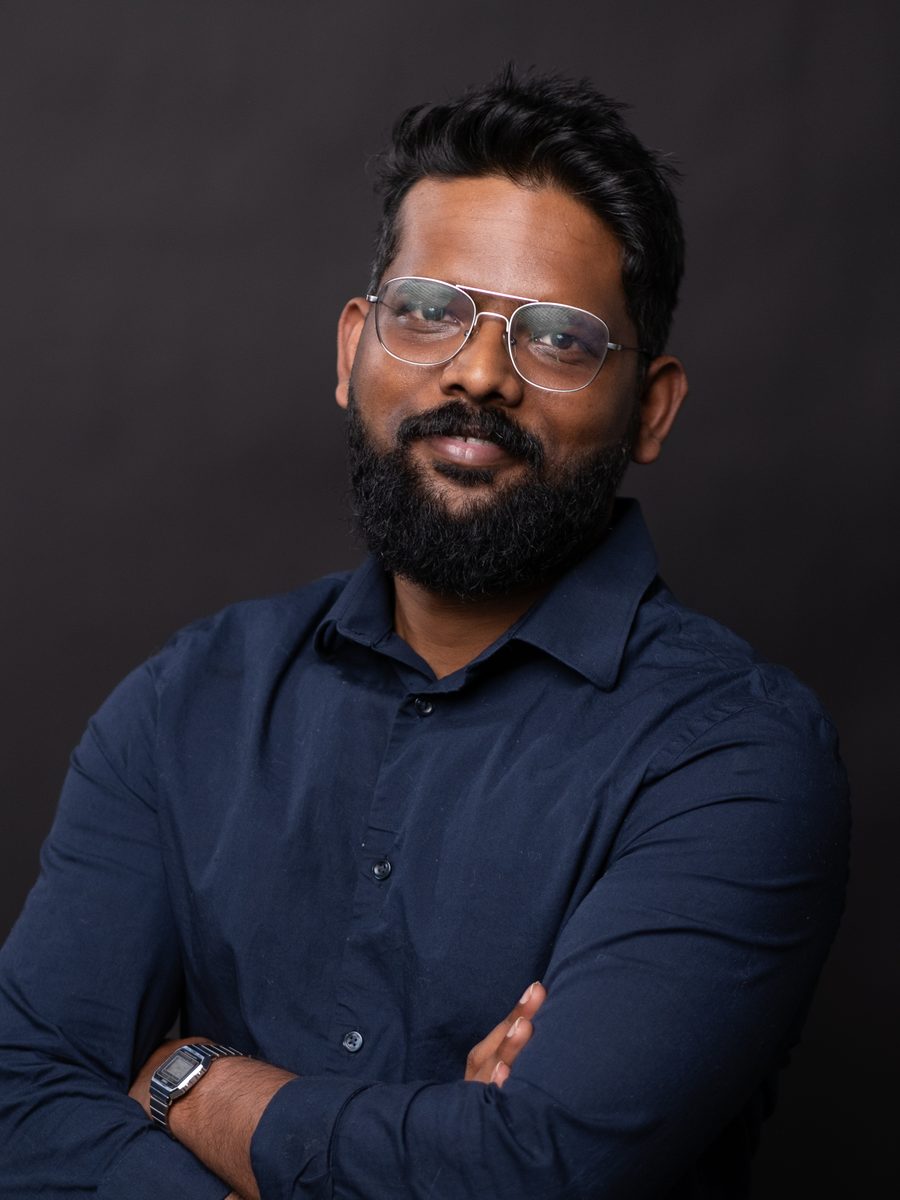 Headshot of a man in glasses with arms crossed on a dark backdrop
