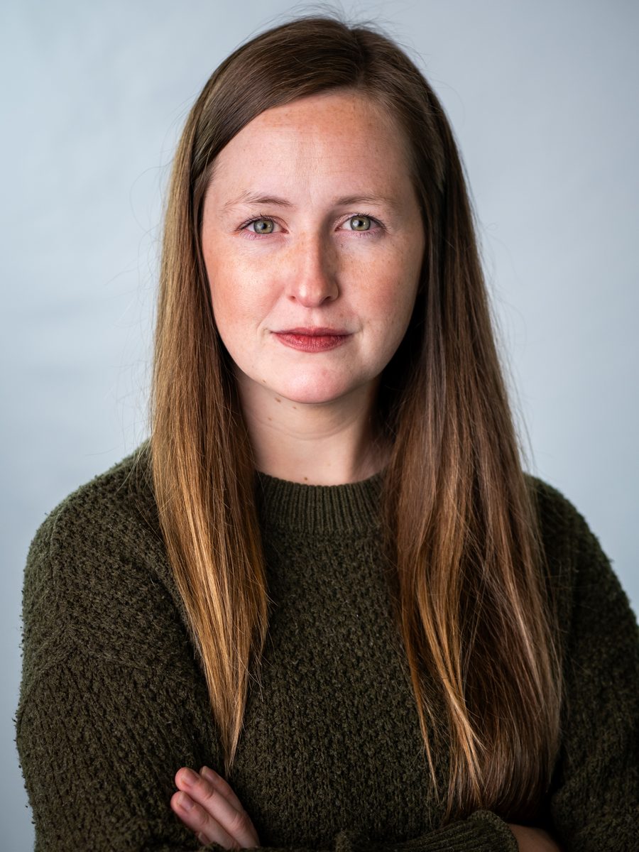 Headshot of a woman in a green sweater on a light blue backdrop