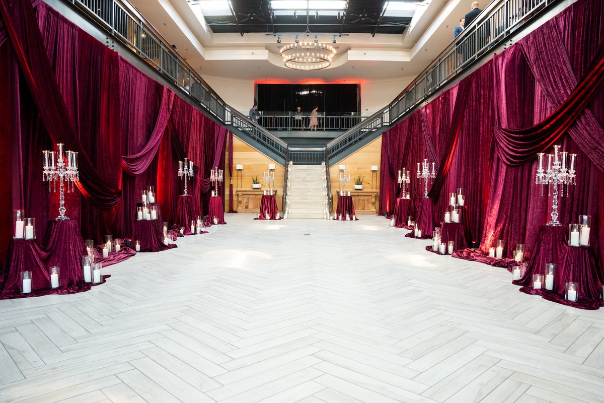 A grand hall lined with red velvet drapes and candlelit tables