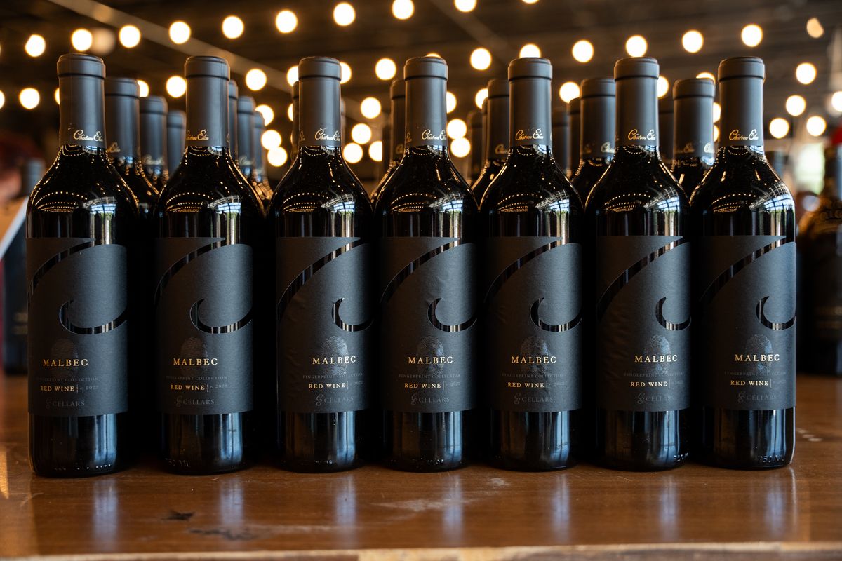 Rows of red wine bottles under warm string lights