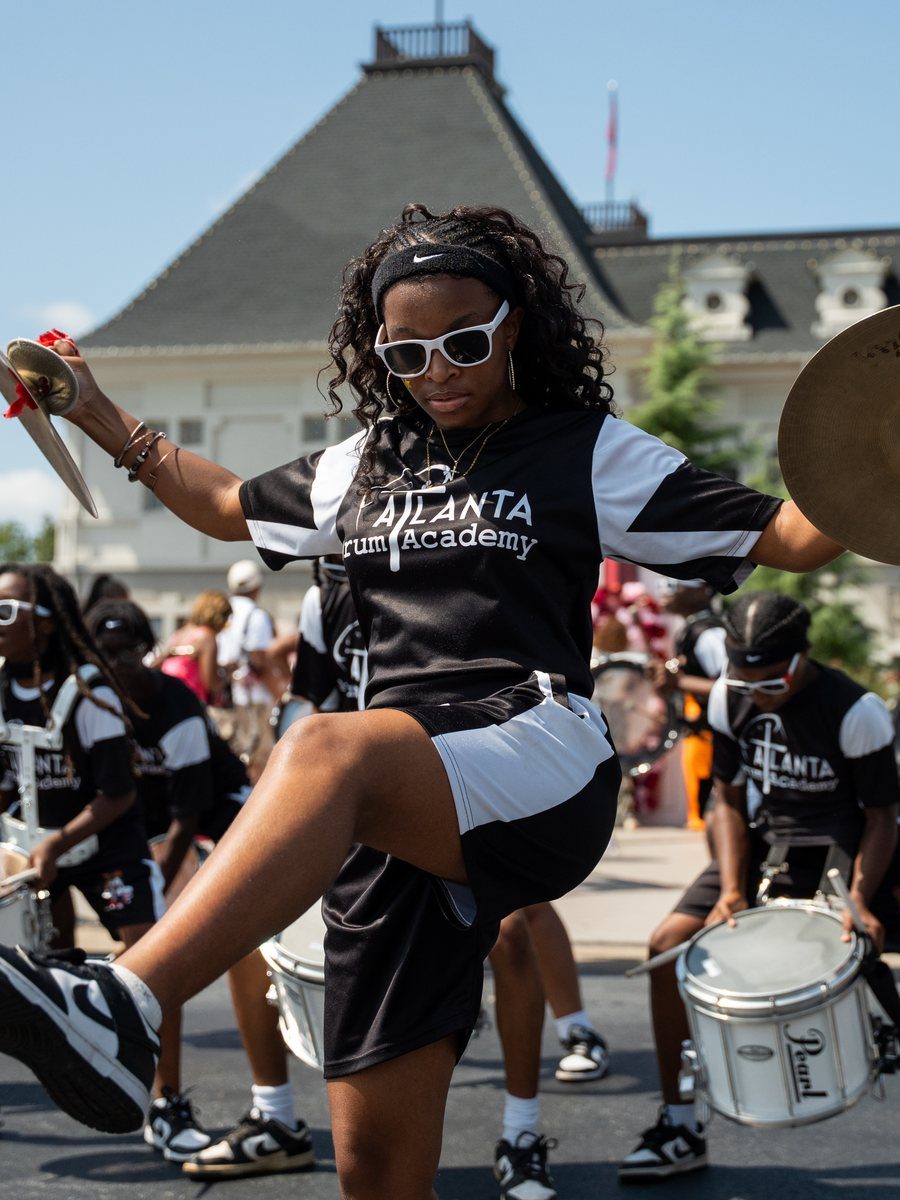 A drumline cymbal player high-kicking in front of the château at Vineyard Fest